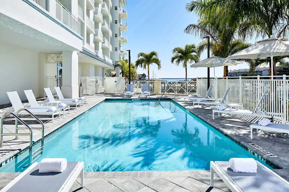 Beachfront pool with crystal blue water, white loungers, umbrellas, and palm trees