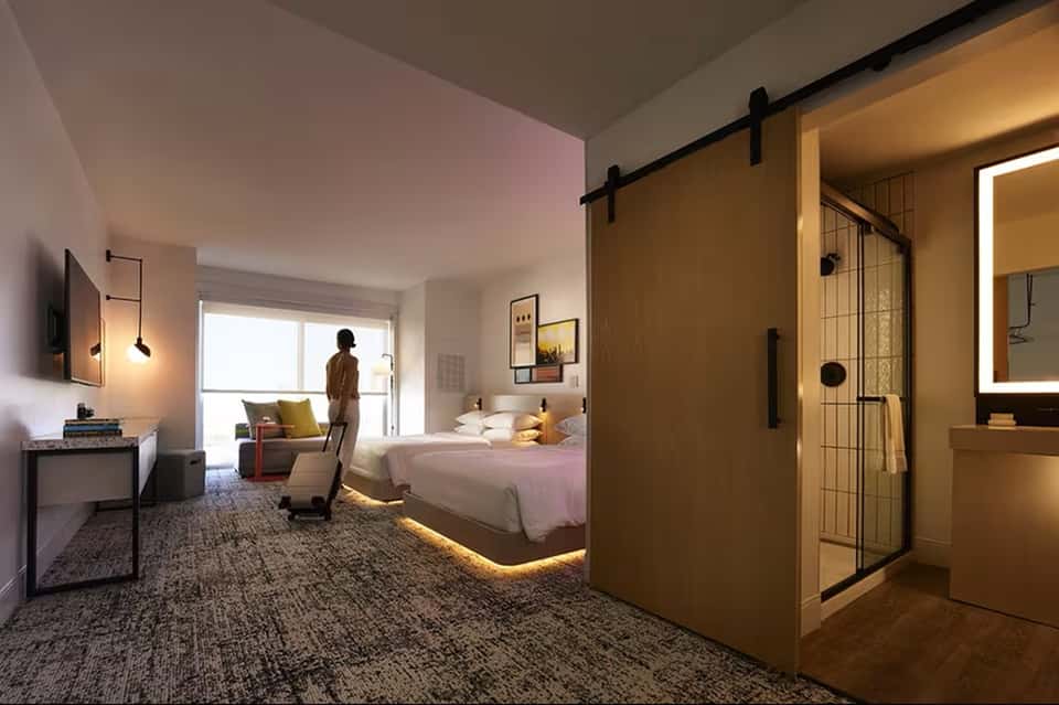 Modern hotel bedroom with king bed, ensuite bathroom with glass shower, and contemporary furnishings