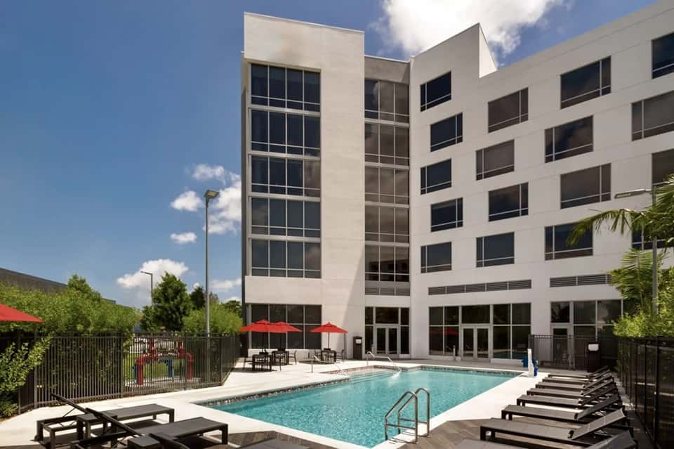 Contemporary white hotel building with pool, black lounge chairs, and red umbrellas in courtyard setting