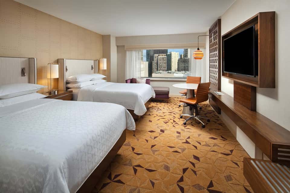 Hotel room with two queen beds, city skyline view through large windows, and business desk
