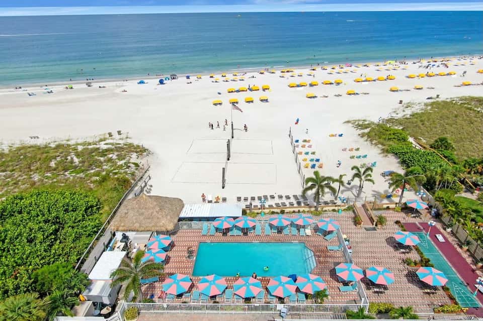 Elevated view of beachfront pool with umbrellas, beach volleyball net, and ocean access
