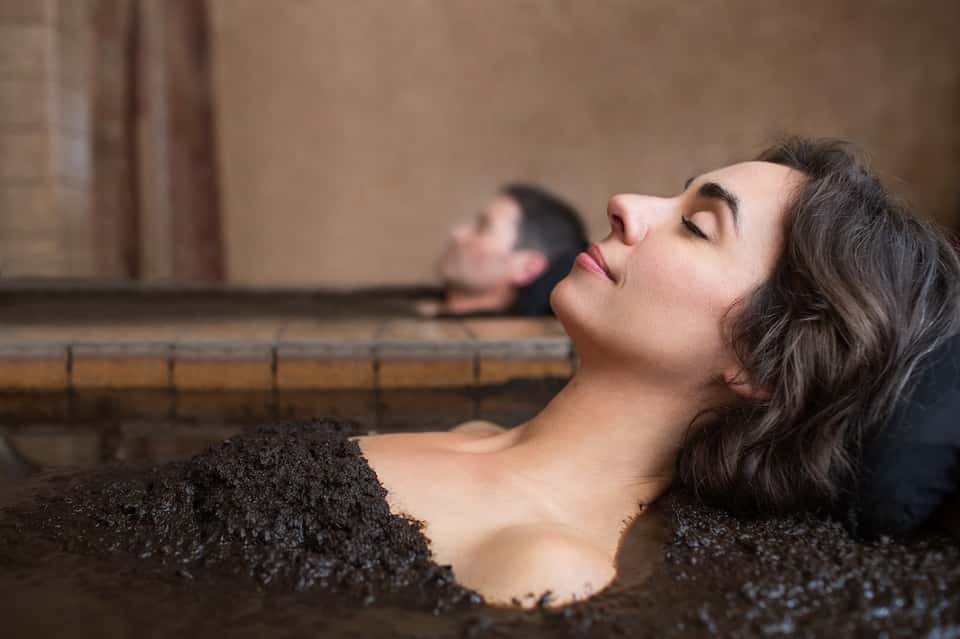 Woman relaxing in thermal spa bath with dark volcanic sand at wellness resort