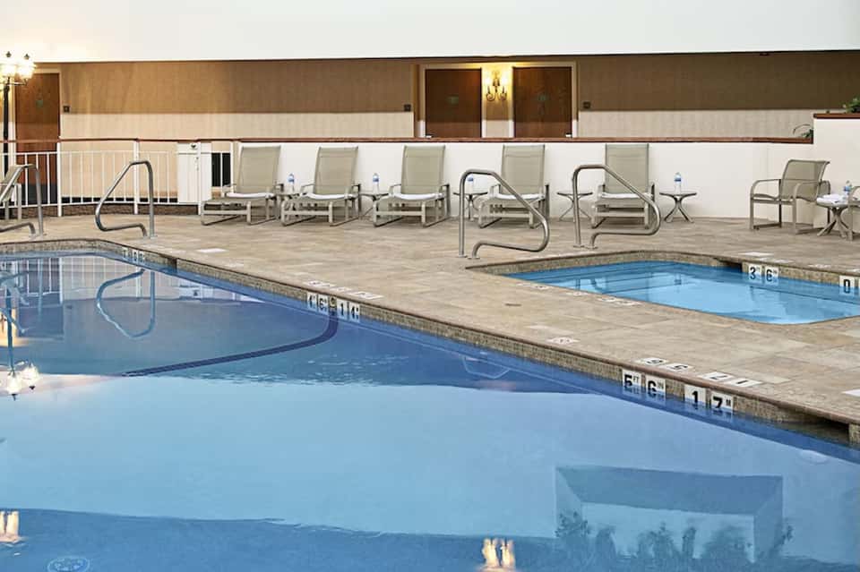 Resort pool deck with two pools, lounge chairs, metal railings, and building with illuminated windows