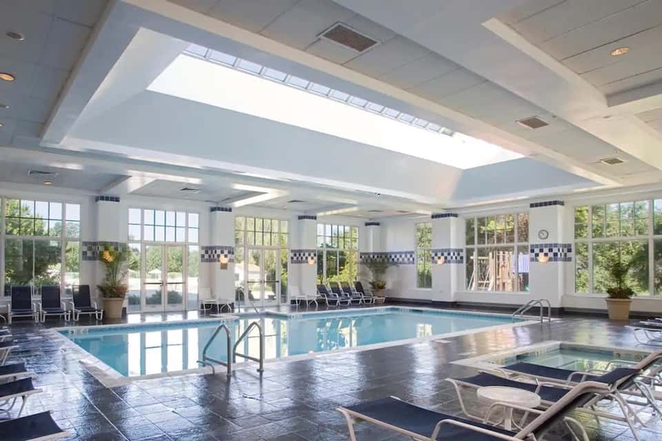 Indoor swimming pool with skylights, lounge chairs, and large windows overlooking gardens