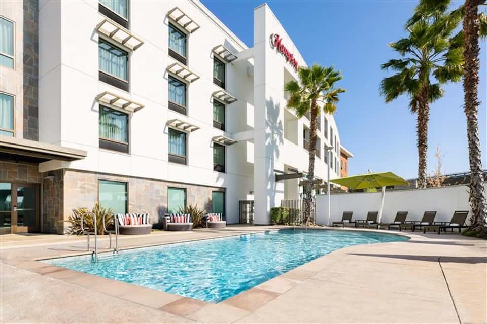 Resort outdoor pool with lounge chairs, palm trees, white building facade, and clear skies