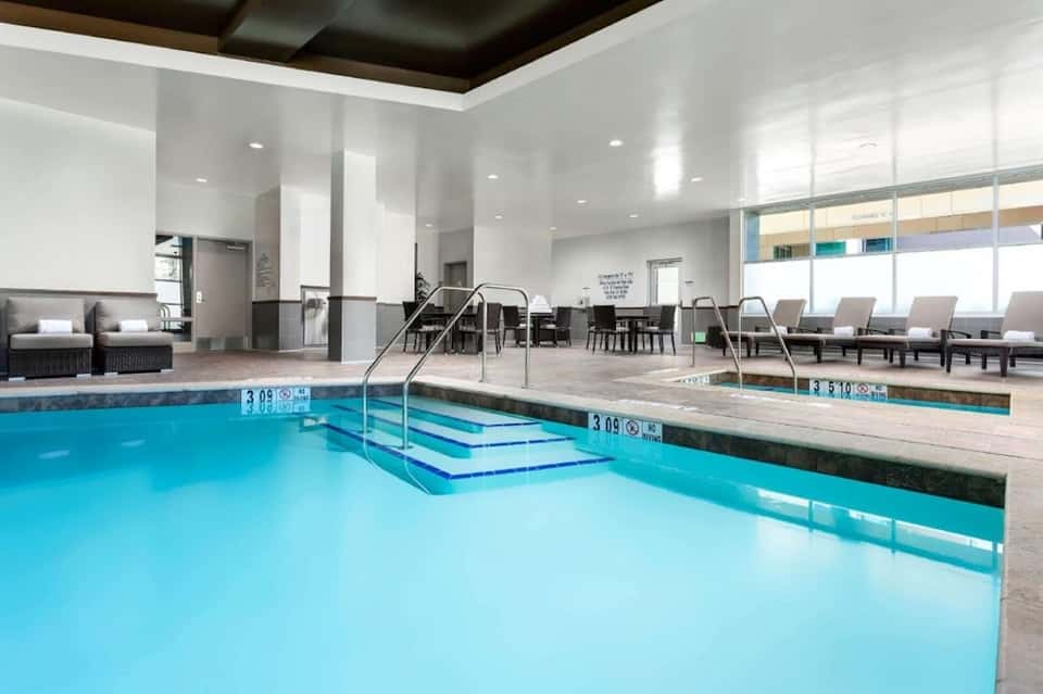 Indoor aquatic center with heated pool, spa, steps, seating area, and large windows