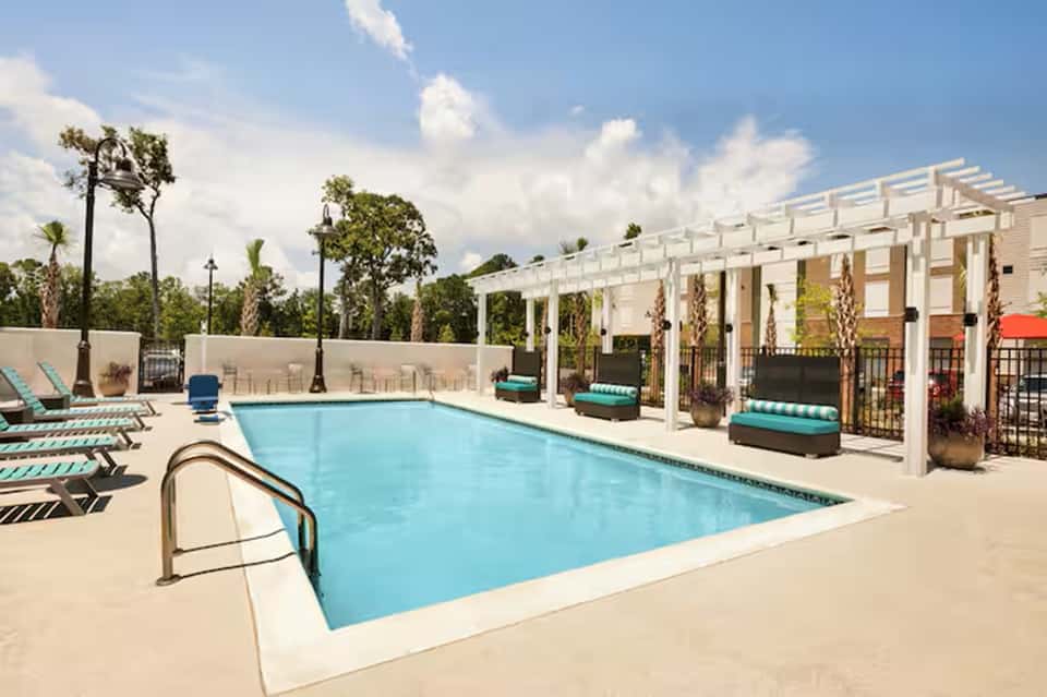 Resort swimming pool with white pergola shade structures and palm tree landscaping