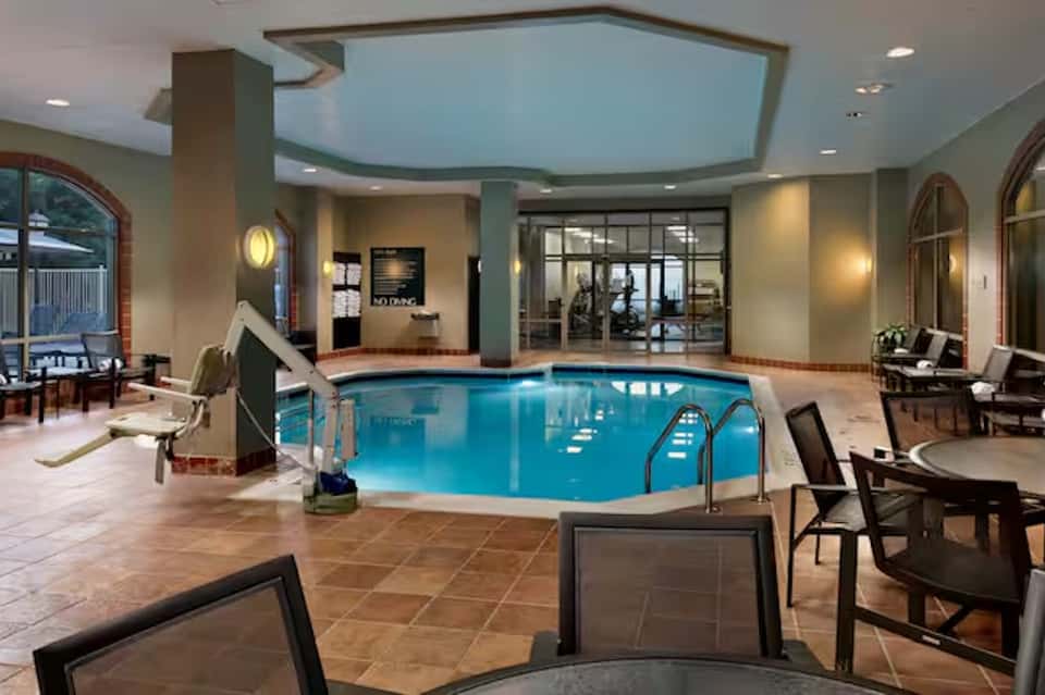 Indoor aquatic center with large heated pool, arched ceiling skylights, seating areas, and elegant tile flooring
