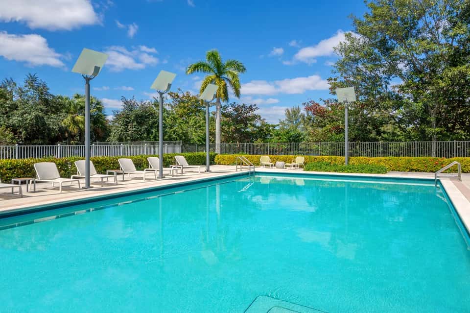 Resort swimming pool with lounge chairs, solar lamps, white fence, and landscaped grounds