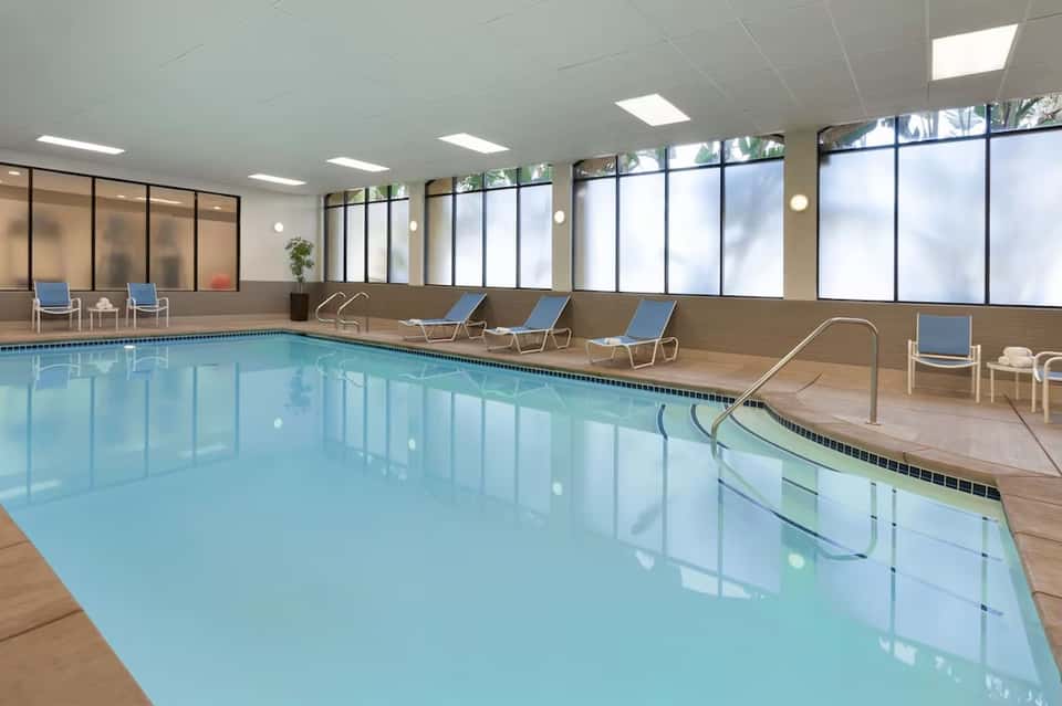 Indoor swimming pool with large windows, blue lounge chairs, and natural light