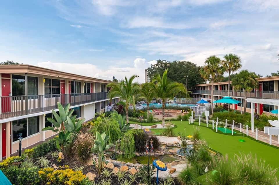 Resort courtyard with colorful motel-style buildings, manicured lawn, pool, and tropical landscaping
