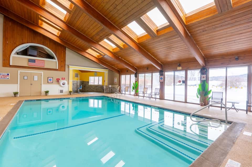 Indoor swimming pool with turquoise water under wood-beamed ceiling with skylights and wide windows