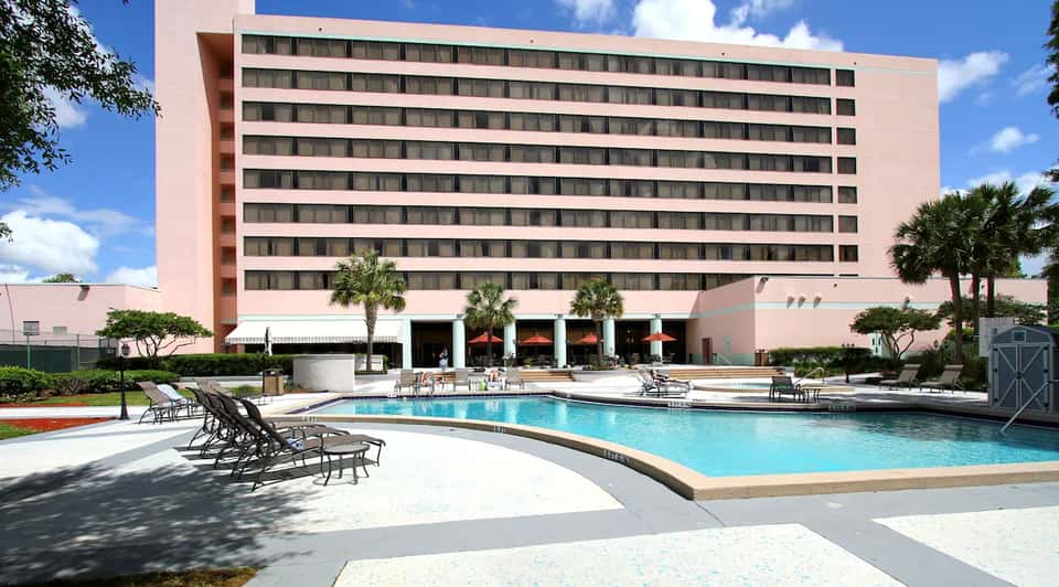 Pink hotel building with pool deck, lounge chairs, and palm trees in sunny weather