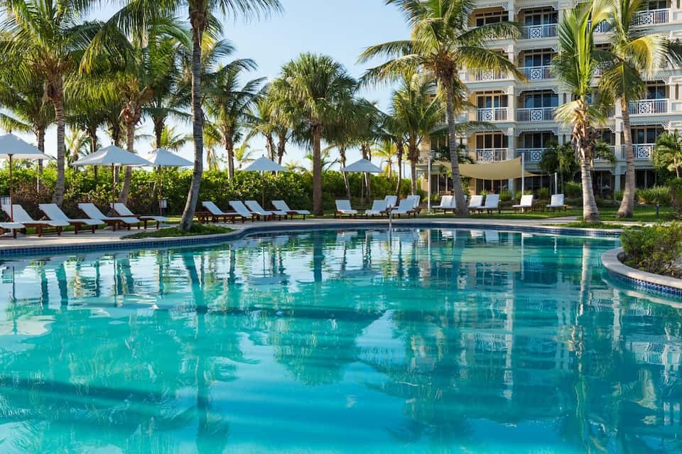 Luxury resort pool surrounded by palm trees, lounge chairs with umbrellas, and elegant building
