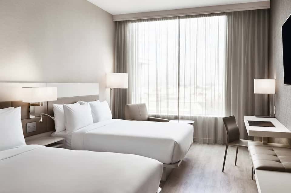 Hotel bedroom with two queen beds, floor-to-ceiling curtains, modern lighting, and contemporary furnishings