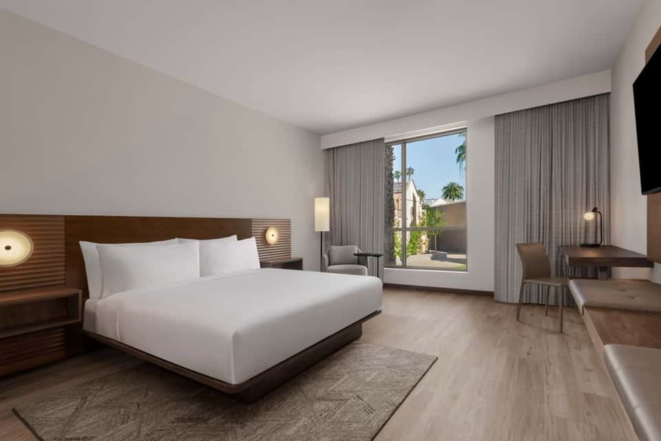 Modern hotel bedroom with king bed, balcony, contemporary furnishings, and warm lighting