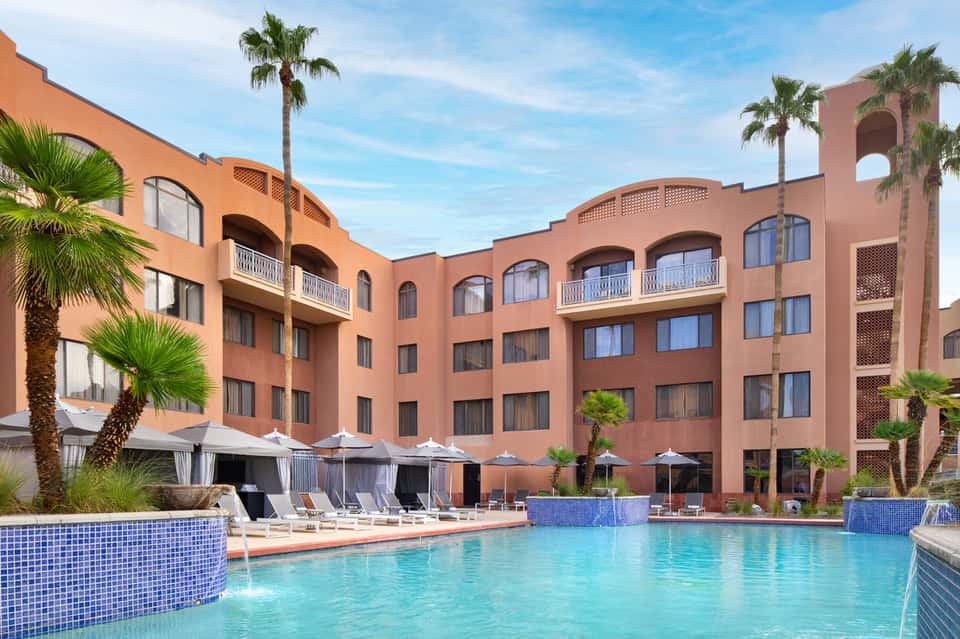 Tropical resort pool with terracotta architecture, palm trees, and lounge seating