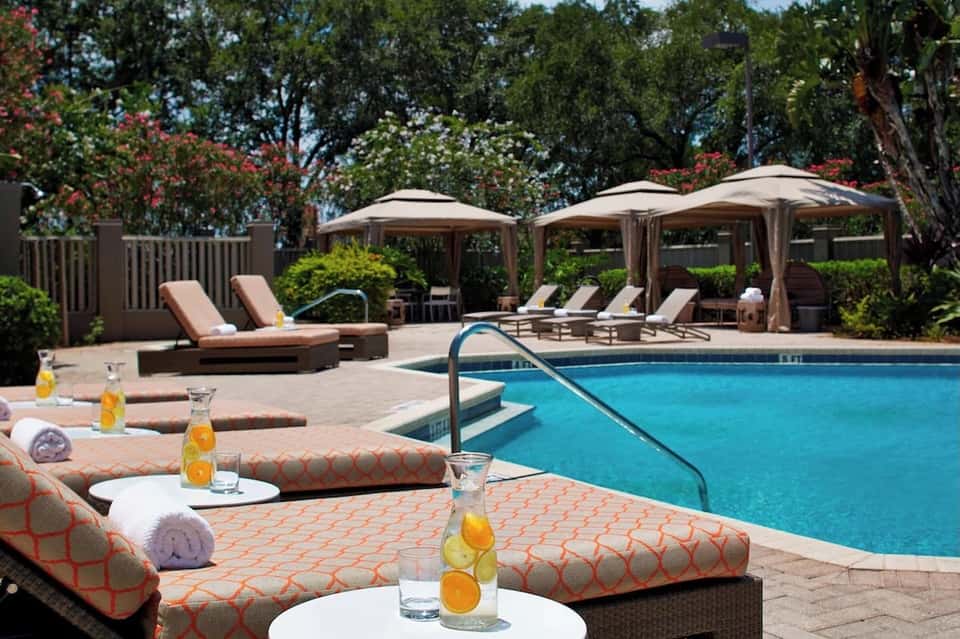 Resort pool surrounded by lounge chairs, cabanas, lush landscaping, and beverages