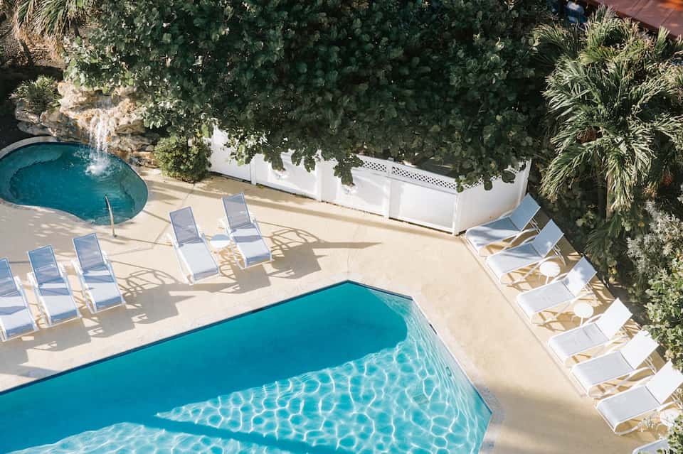 Resort pool with turquoise water, lounge chairs with white cushions, and lush green vegetation