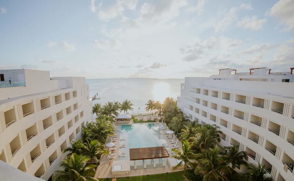 Beachfront resort aerial view with central pool, palm trees, and ocean backdrop