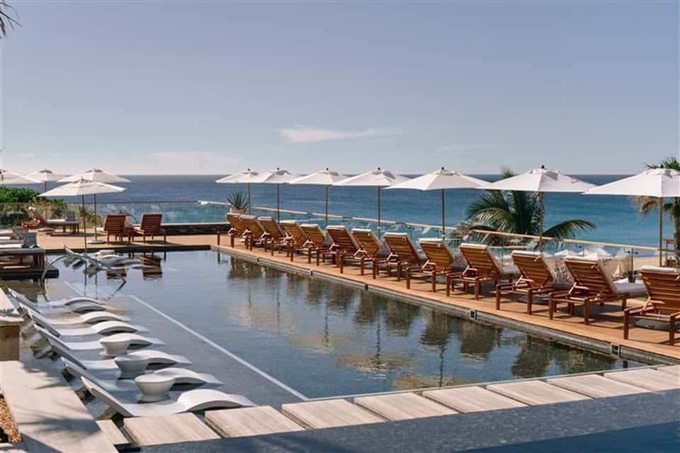 Beachfront infinity pool with ocean views, lounge chairs, and white umbrellas