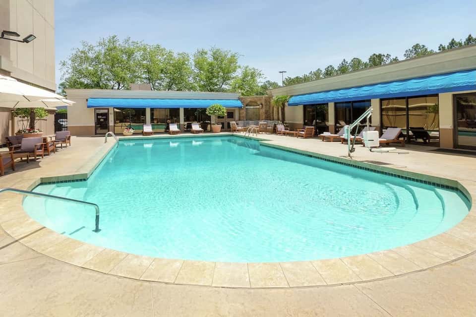 Resort swimming pool with blue retractable shade covers and lounge seating on patio