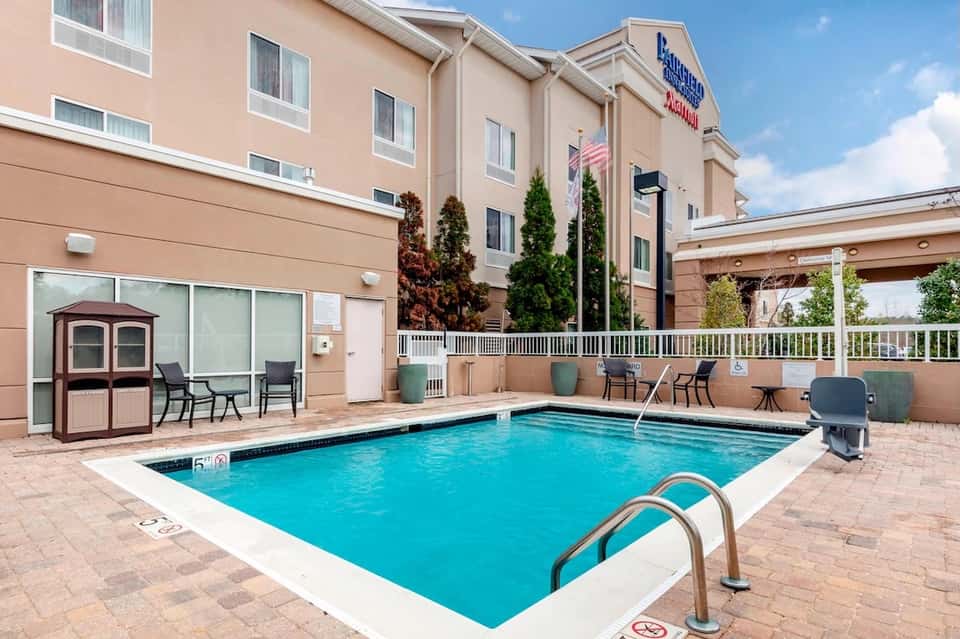 Hotel outdoor pool with blue water, white deck, lounge chairs, and attached hotel building facade