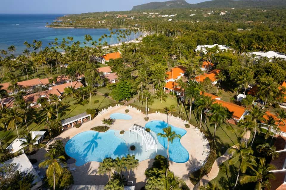 Aerial view of tropical resort with blue pools, palm trees, and ocean coastline