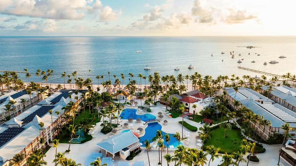 Beachfront resort aerial view with blue pools, palm trees, ocean, and sandy beach