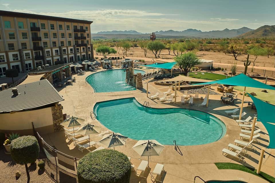 Desert resort pool complex with multiple pools, turquoise water, cabanas, mountains, and arid landscape