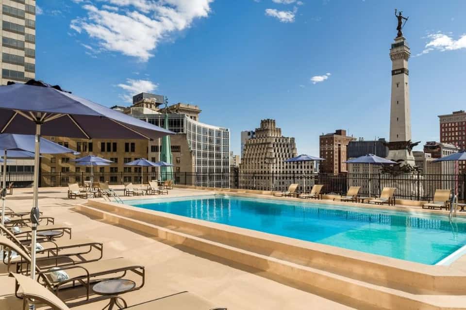 Rooftop pool in urban setting with city skyline, blue umbrellas, and lounge chairs