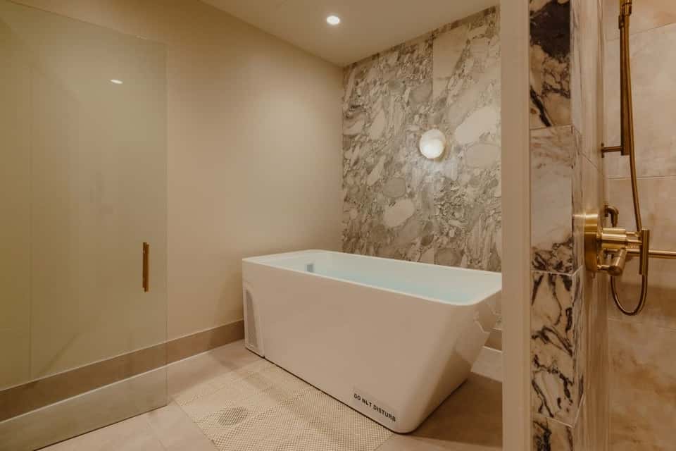 Luxurious spa bathroom with freestanding white tub, marble feature wall, and gold fixtures
