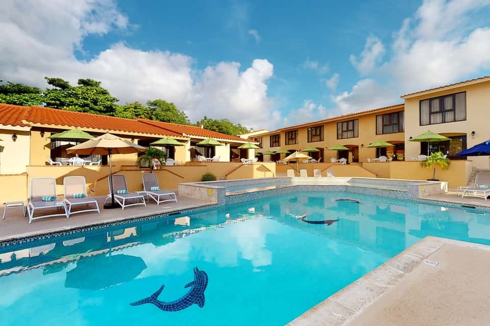 Tropical resort pool with mosaic tile design, loungers, yellow umbrellas, and Spanish-style architecture