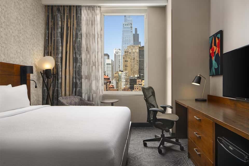 Hotel bedroom with city skyline view through floor-to-ceiling windows