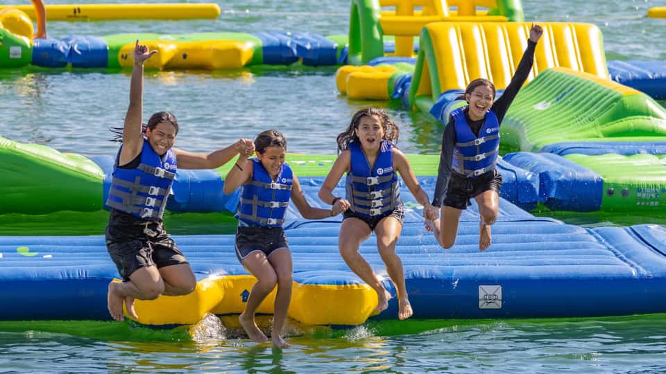 Children in life vests playing on colorful inflatable water park obstacles in ocean