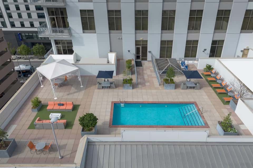 Rooftop pool deck with turquoise pool, lounge chairs, white tent, and urban courtyard view