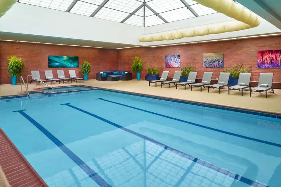 Indoor lap pool with lane markers, skylights, lounge chairs, and brick walls