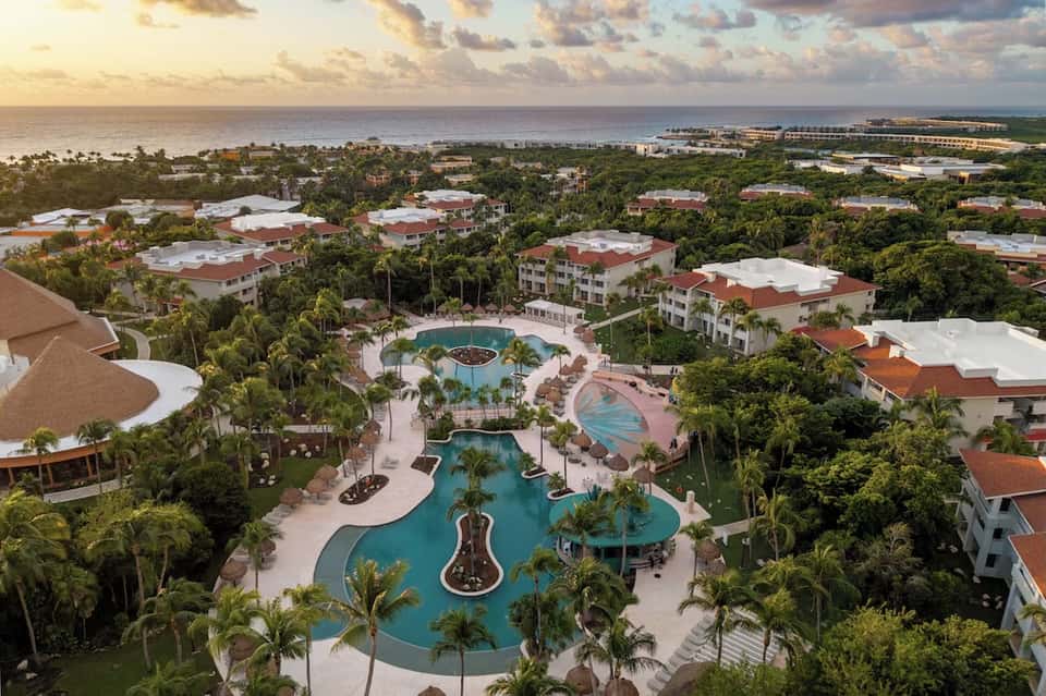 Aerial view of beachfront resort with multiple pools, palm trees, and coastal landscape