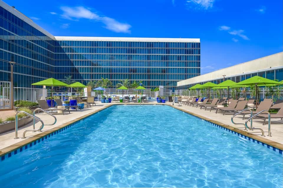 Modern hotel outdoor pool with blue umbrellas, lounge chairs, high-rise building backdrop