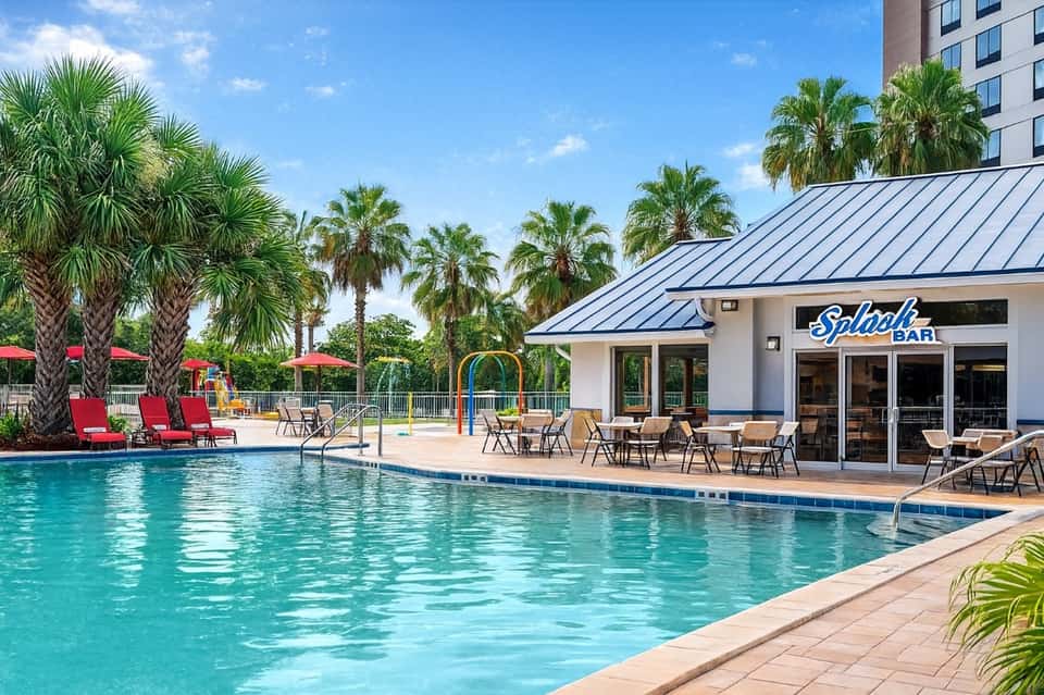 Resort pool with turquoise water, red lounge chairs, palm trees, and Splash Bar pavilion