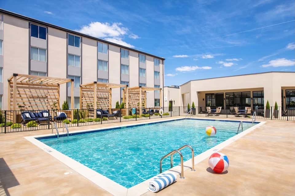 Resort outdoor pool with wooden pergolas, lounge chairs, and hotel building in background