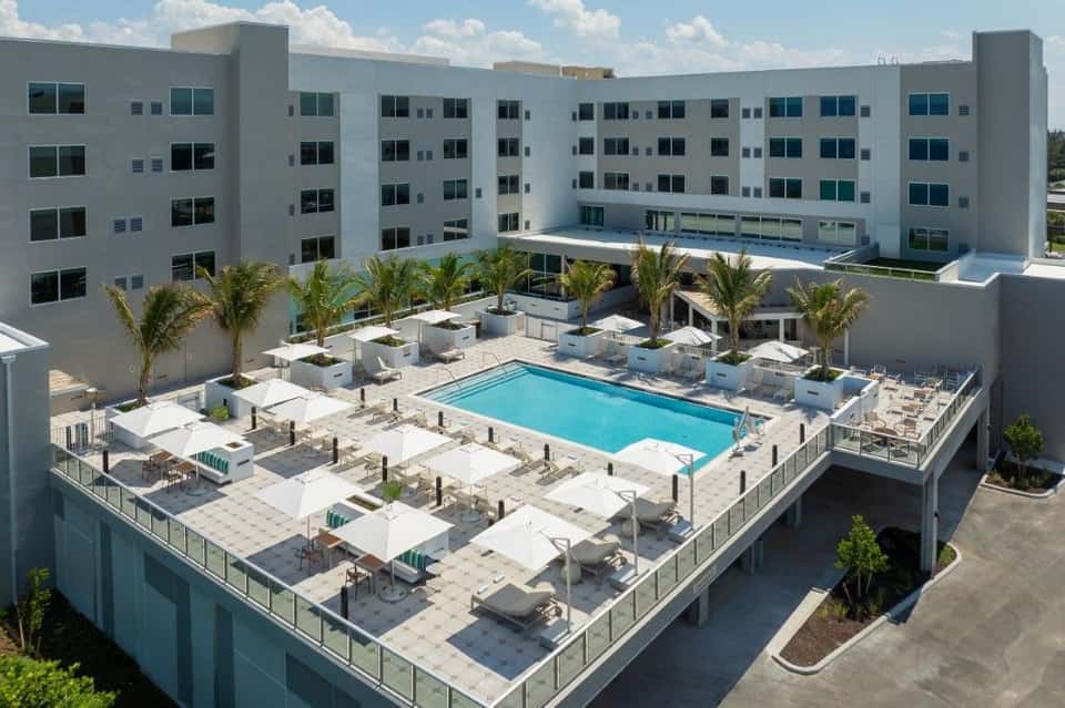 Modern white apartment complex with central pool and palm trees surrounded by lounge chairs