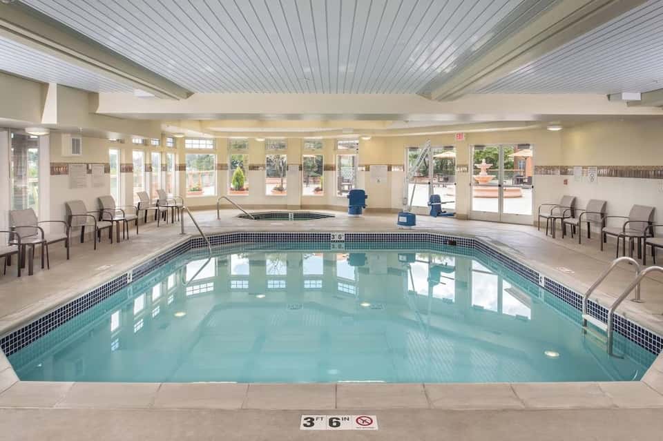 Indoor heated swimming pool with aqua water, comfortable seating, and bright natural light from windows