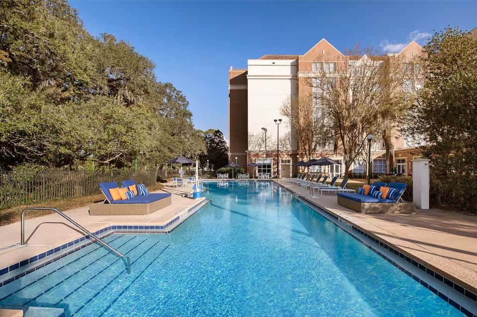 Resort outdoor pool with blue water, lounge chairs, striped cushions, and hotel building backdrop