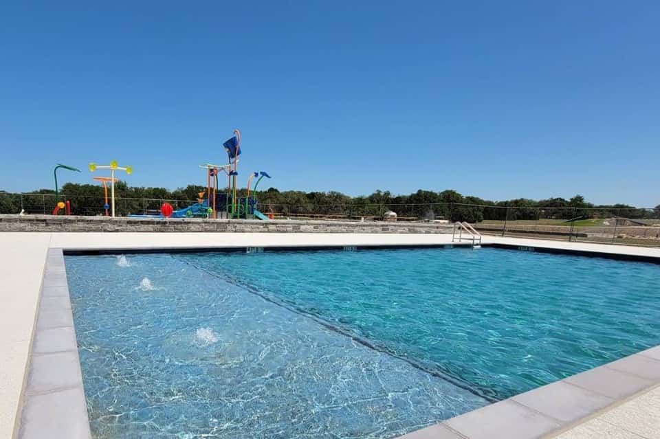 Resort swimming pool with water slide and playground structure visible in background under clear sky