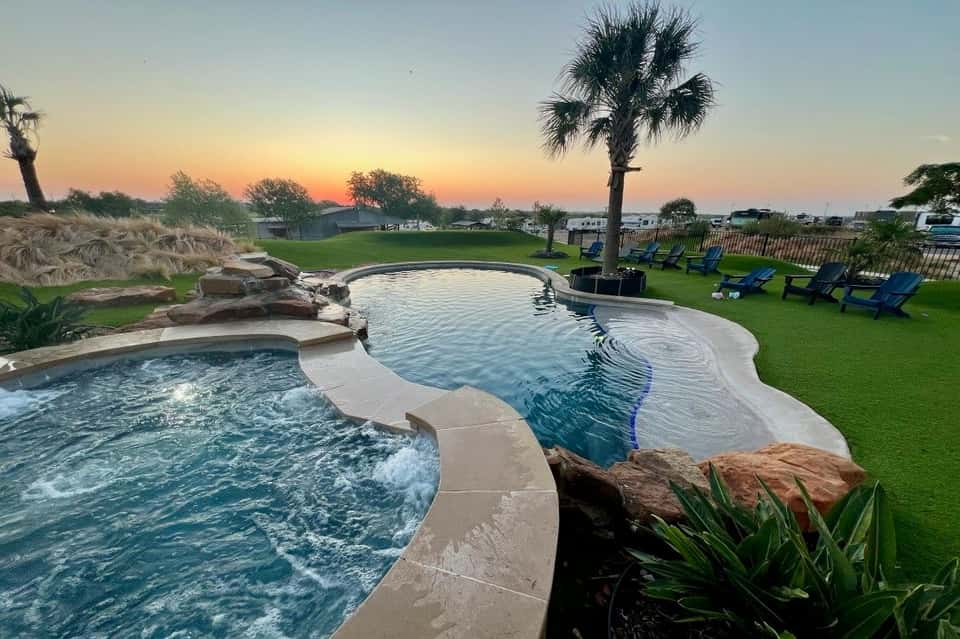 Two connected resort pools with spa jets, stone waterfall, palm tree, and sunset landscape view