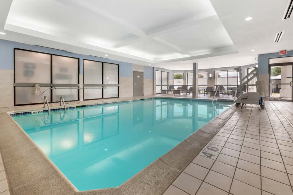 Indoor heated saltwater pool with large windows, white coffered ceiling, and ocean view access