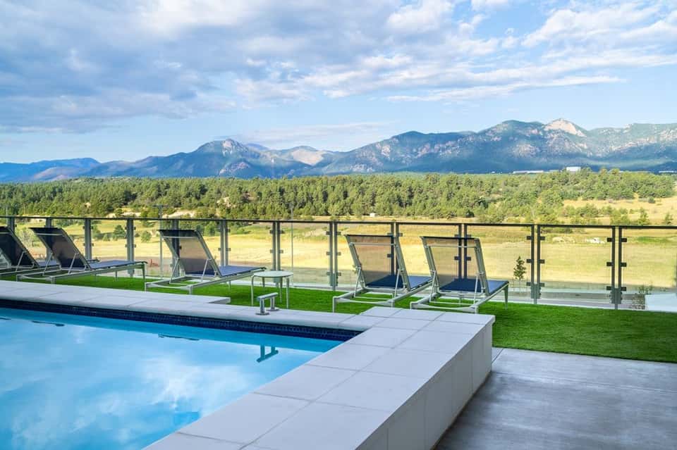 Modern resort pool with loungers, glass railing, and mountain range vista beyond