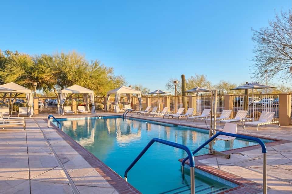 Resort pool with loungers and cabanas under clear blue sky surrounded by desert landscaping