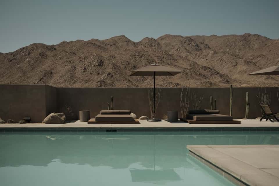 Luxury resort pool with turquoise water, desert mountain backdrop, and minimalist lounge seating